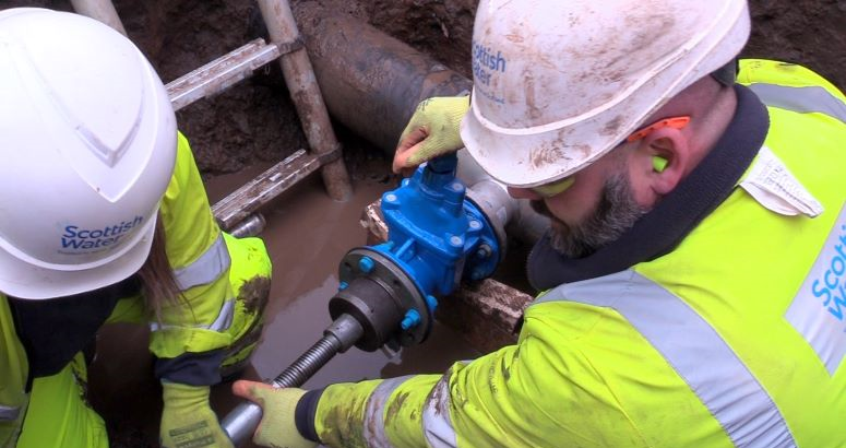 Two Scottish Water engineers work on exposed pipes