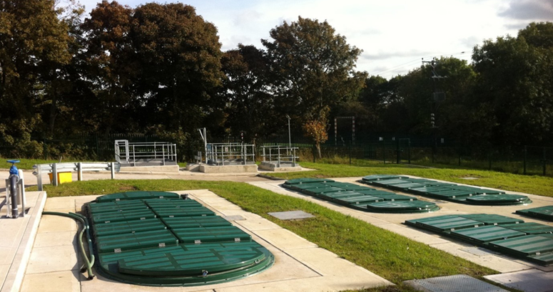 a waste water treatment site showing infrastructure with trees in the background