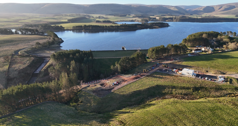 Gladhouse Reservoir Site Compound and Construction Site An aerial view of a construction site near a large body of open water with surrounding green landscape.