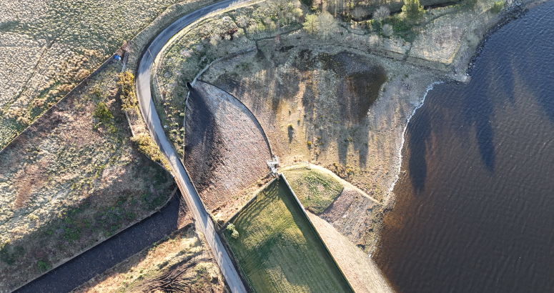 Gladhouse Reservoir Road Bridge Aerial view of a curving road alongside a dam, with water on one side and a rugged landscape on the other.