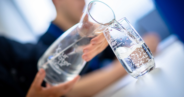 Hand with a Your Water Your Life branded jug filling up a glass with Scottish Water printed on it