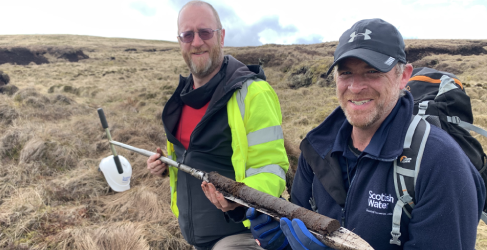 Two Scottish Water workers holding up dirt from the bog