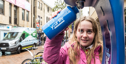 Young girl holding water bottle under Top up tap