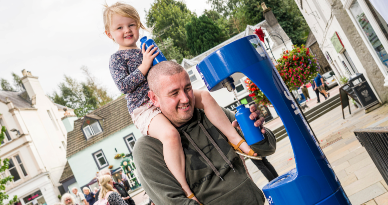 A father carries his small daughter on his shoulders while filling a bottle from the new top up tap