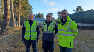 Three men stand in the yard at Ballater Water Treatment Works. They are wearing hi-vis jackets.
