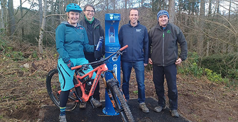 Group of people at water tap with bike and trees