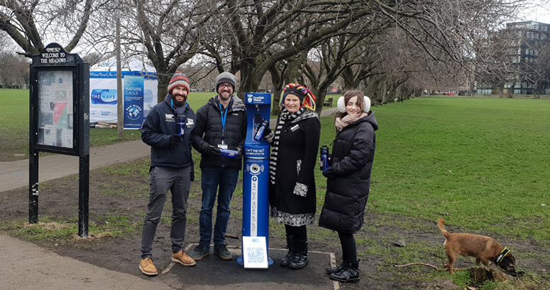 People standing in park next to blue water refill tap