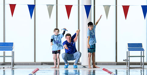 Man and children standing beside a swimming pool