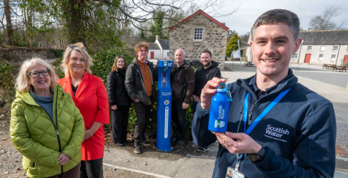 A group of councillors and staff from Aden Country Park surround a blue outdoor Scottish Water top-up tap. On the right of the picture is a Scottish Water employee holding a blue metal branded water bottle.