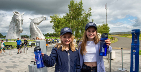 Two girls holding water bottles with Kelpies sculpture in background