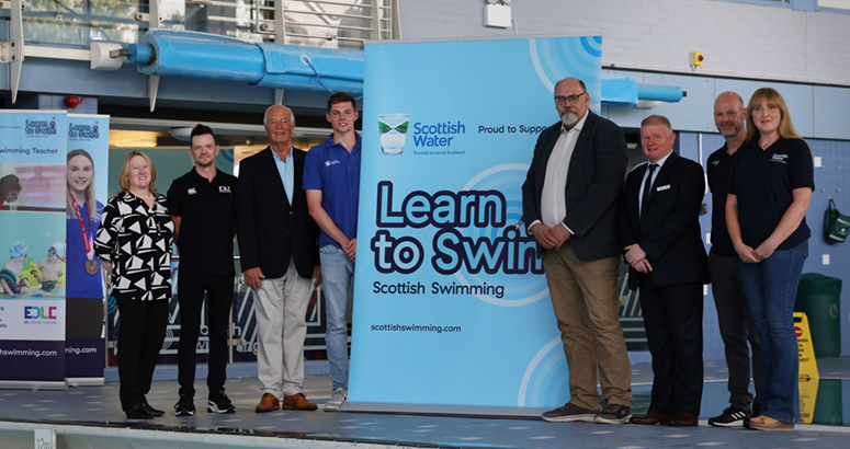 People posing around large Learn to Swim banners