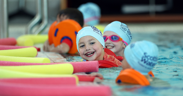 Learn to Swim design a swim cap competition children in swimming pool with smiling face of two, using floats and wearing swim caps