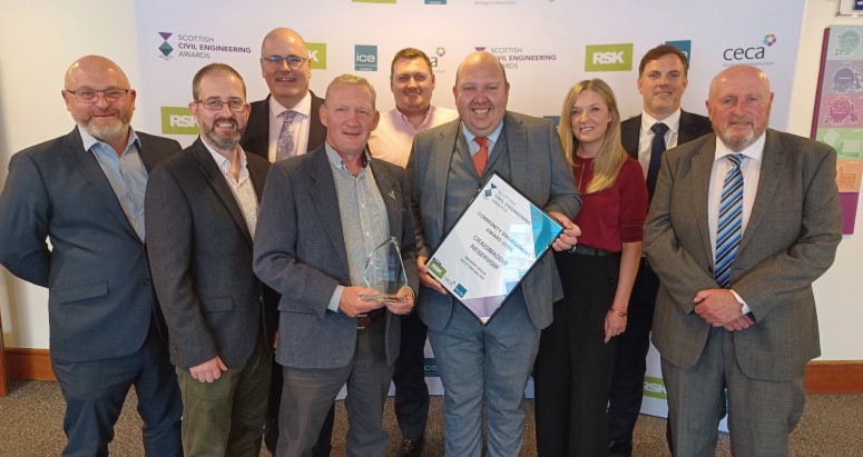 2025 Scottish Civil Engineering Awards Group of nine people posing with an award at an event. Some are smiling and holding a certificate and a trophy. The setting suggests a professional or corporate event.