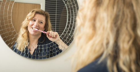 Woman brushing teeth in mirror