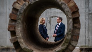 Alex Plant and Deirdre Michie posing through water pipe Two people pose as camera lense focuses from a far away distance through a water pipe