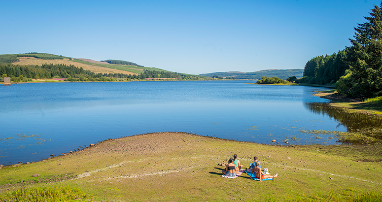 Summer Water Safety 2024 Carron Valley reservoir with group of people sunbathing on the shore on a sunny day