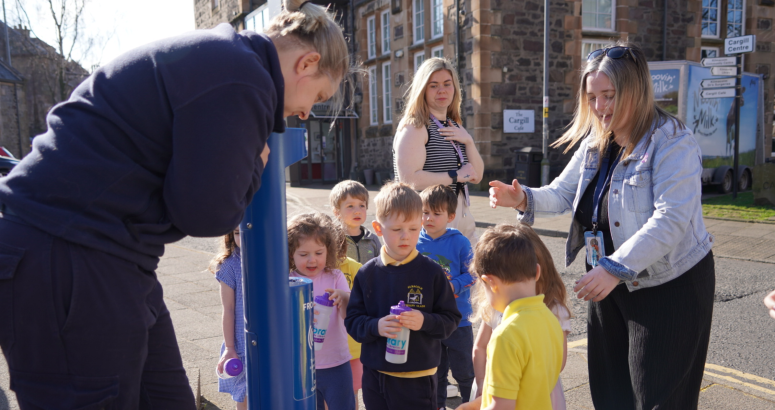 Nursery children topping up from the tap 