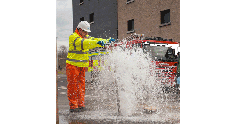 Man in PPE standing in front of water coming out a fire hydrant